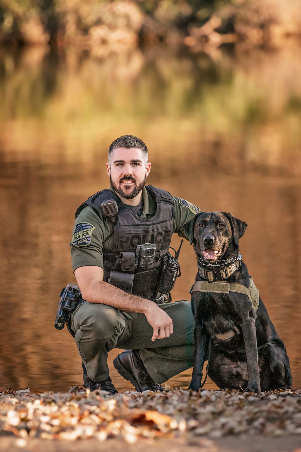 A law enforcement K9 and handler posing together by a lake.