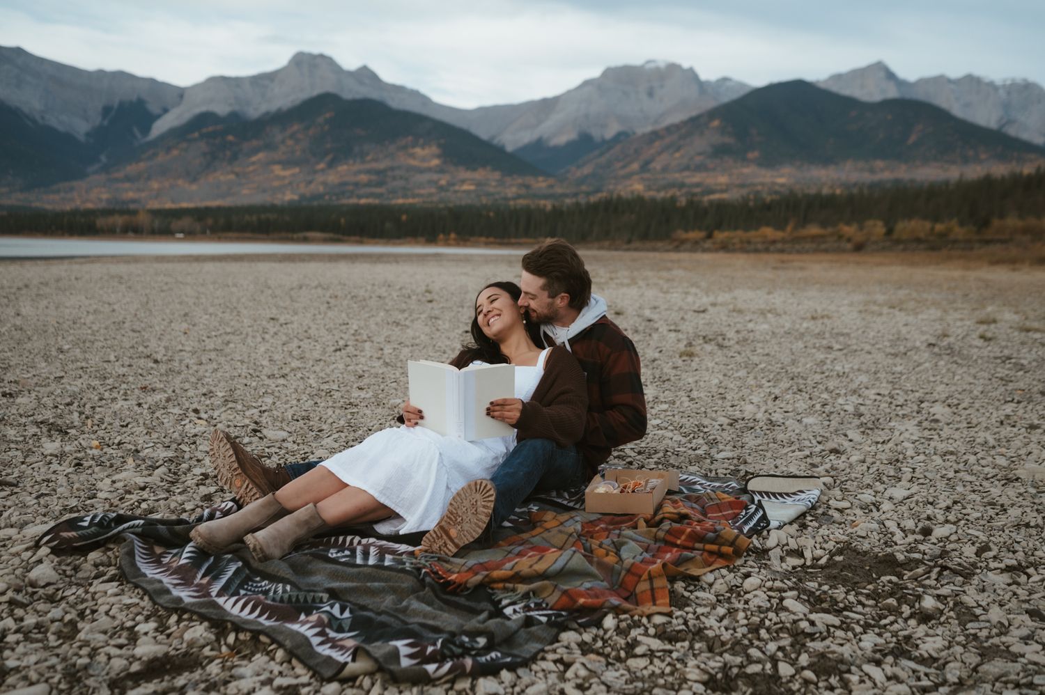 Romantic picnic on a rocky beach with mountain views and a blanket laid out.