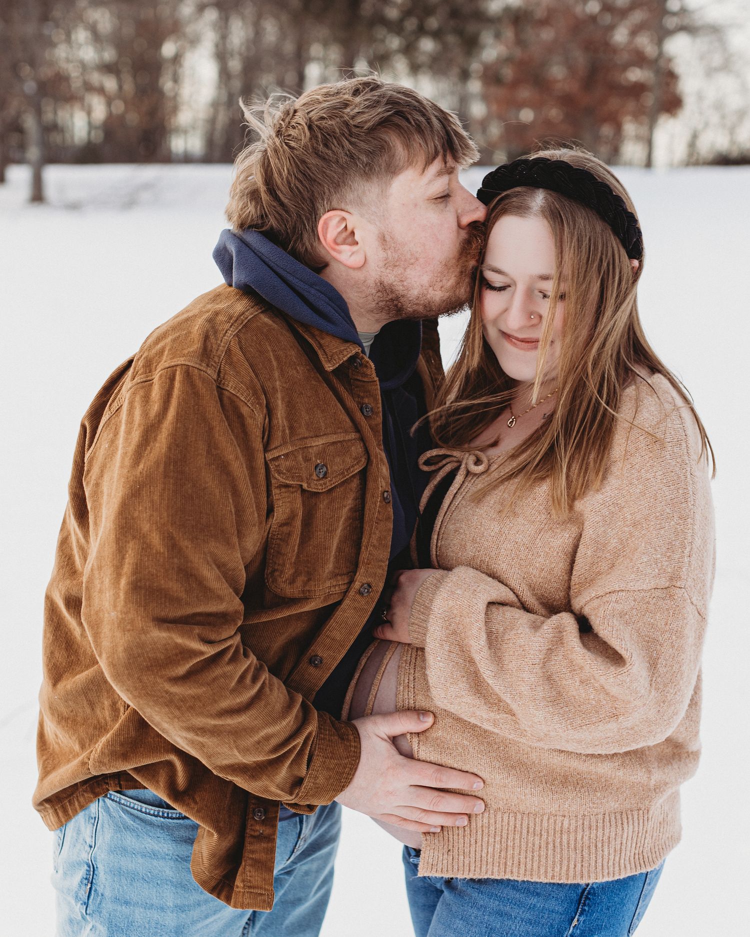 Winter maternity couples photo in Maine with expecting parents embracing in snowy landscape at golden hour