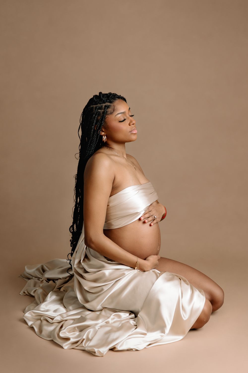 mom wrapped in golden fabric kneeling on mocha colored backdrop