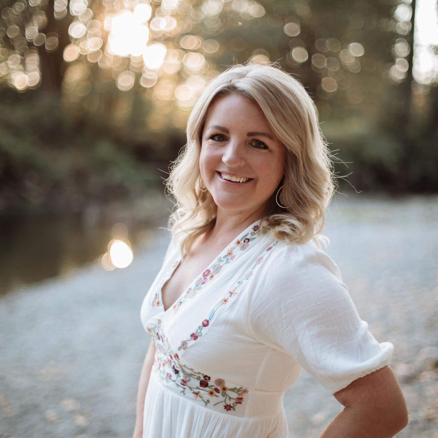 A woman in white embroidered dress poses outdoors during golden hour.
