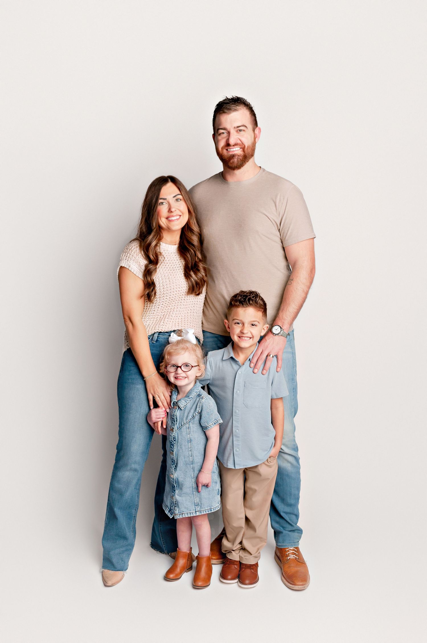 Family of four posing in coordinated neutral outfits in bright white studio portrait.