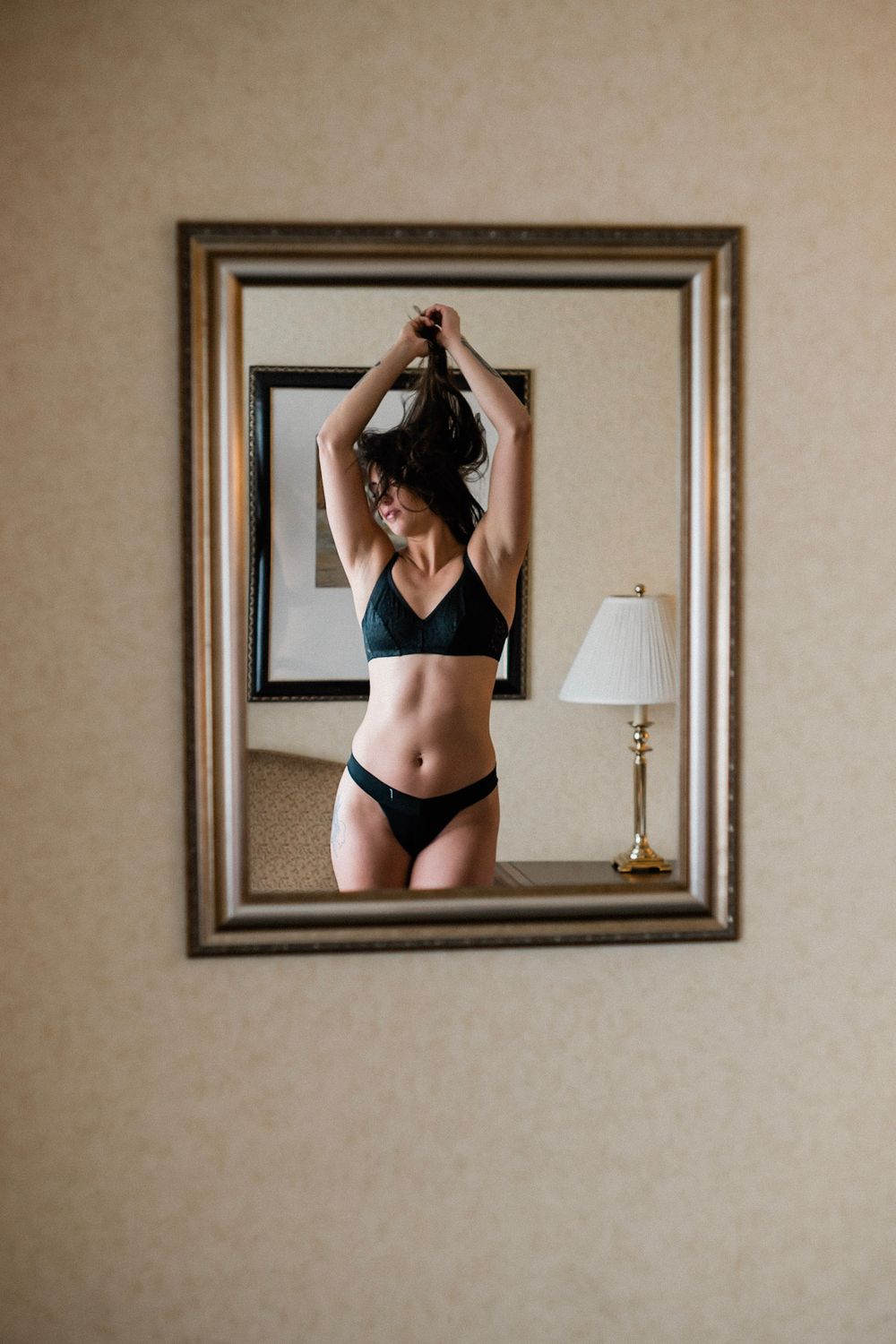 A series of mirror self portraits showing a figure in black undergarments against a beige wall with framed artwork.
