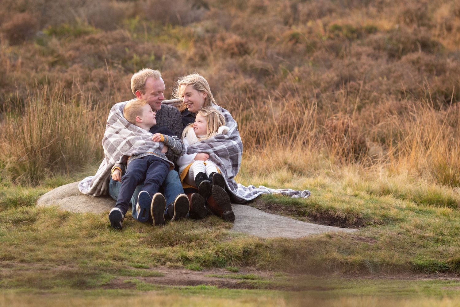 Couple wrapped in blankets share intimate moment on hillside at sunset.