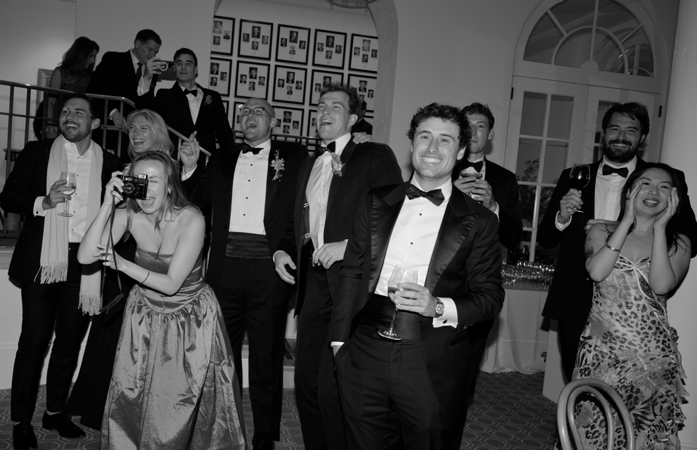 Elegant black and white photo of guests in formal attire at a gala event, laughing and socializing indoors.