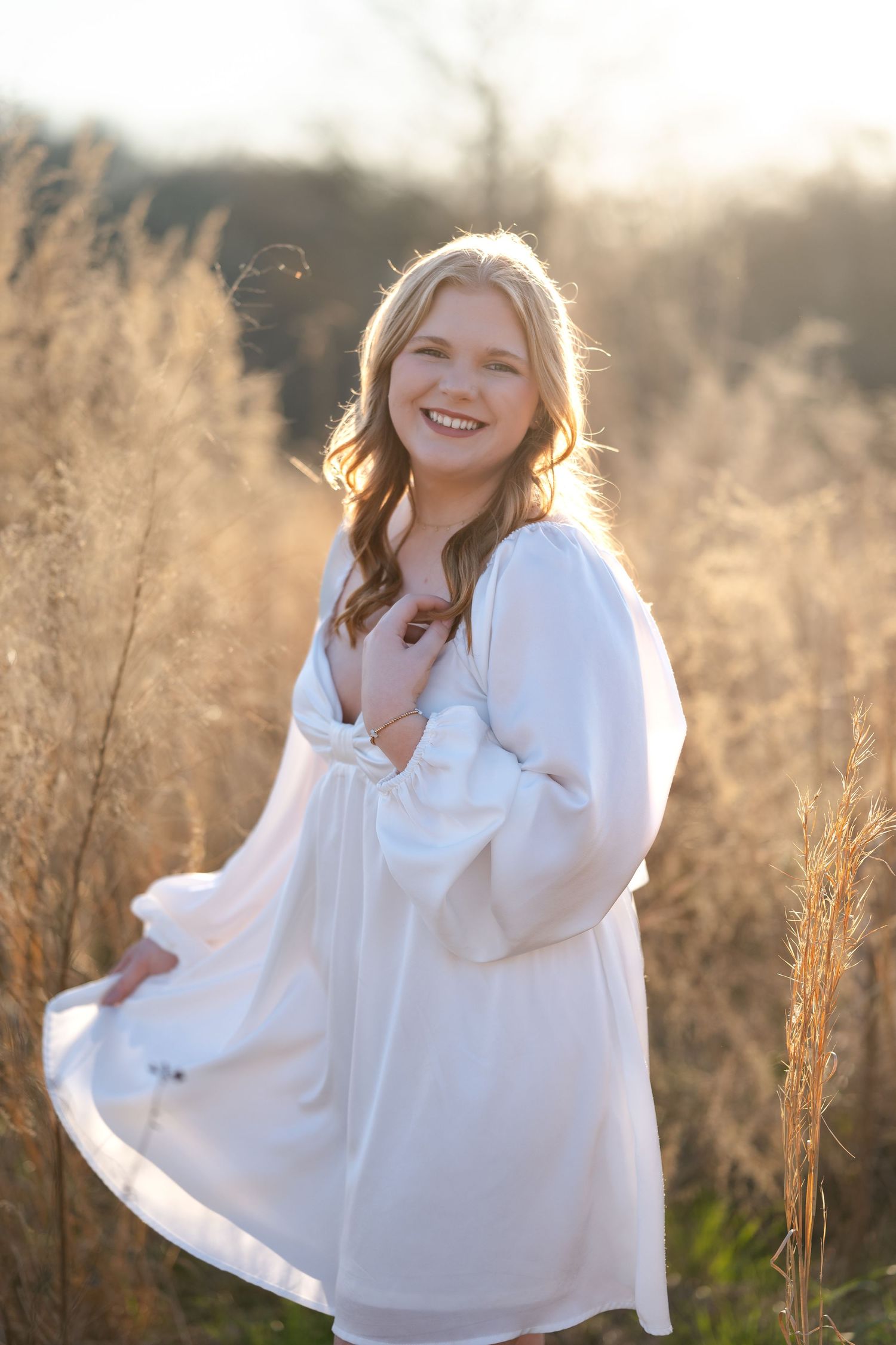 Joyful outdoor portrait in flowing white dress surrounded by sunlit tall grass.