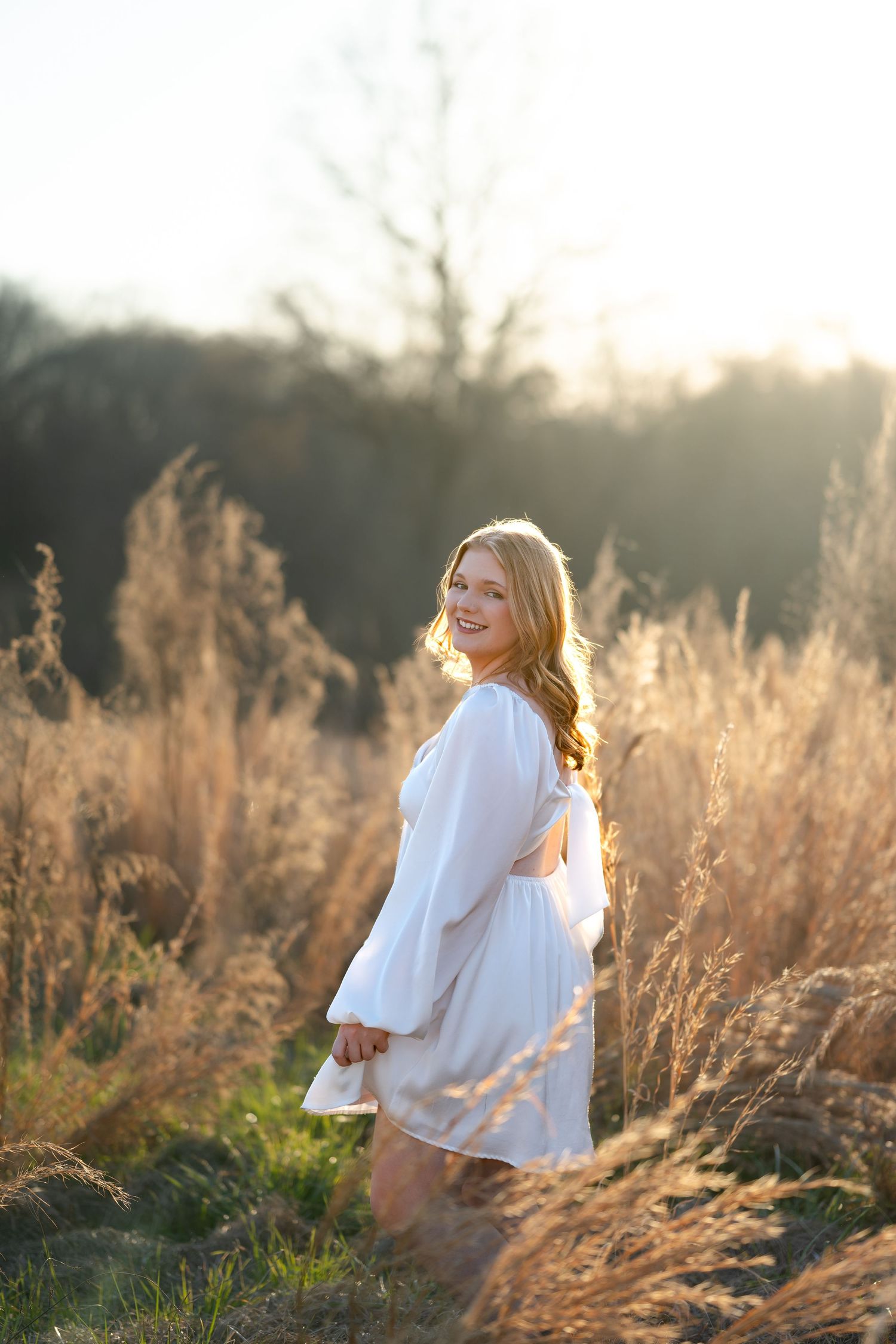 A dreamy portrait in a white dress among tall grasses during golden hour.