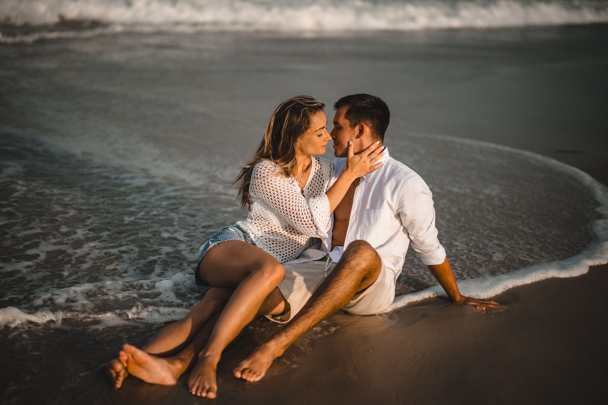 Romantic intimate pose of a couple sitting together in the waves edge at island beach state park at sunset