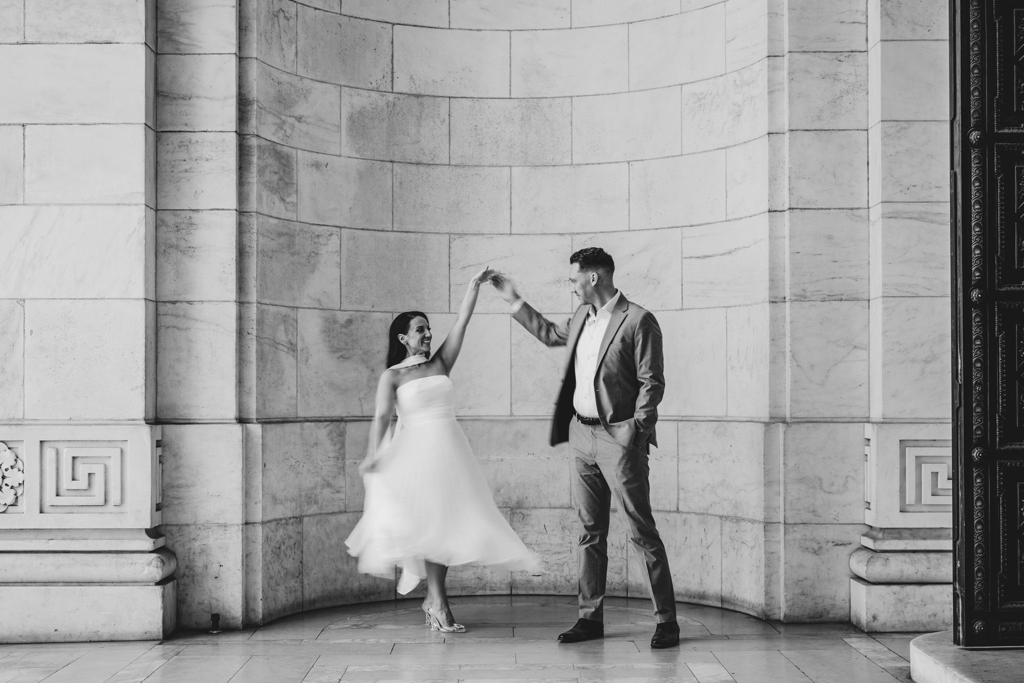 A romantic black and white dance pose between a couple in formal attire against a stone arch at new york public library