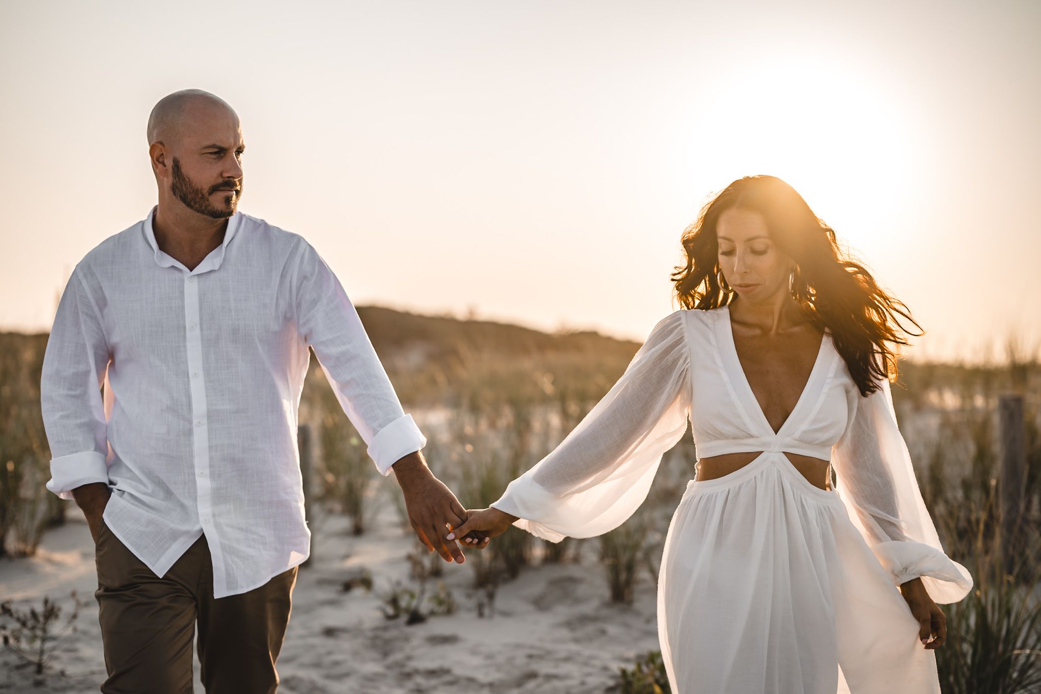 engagement session images of a Couple walking hand in hand along island beach state park sandy beach path during golden hour sunset