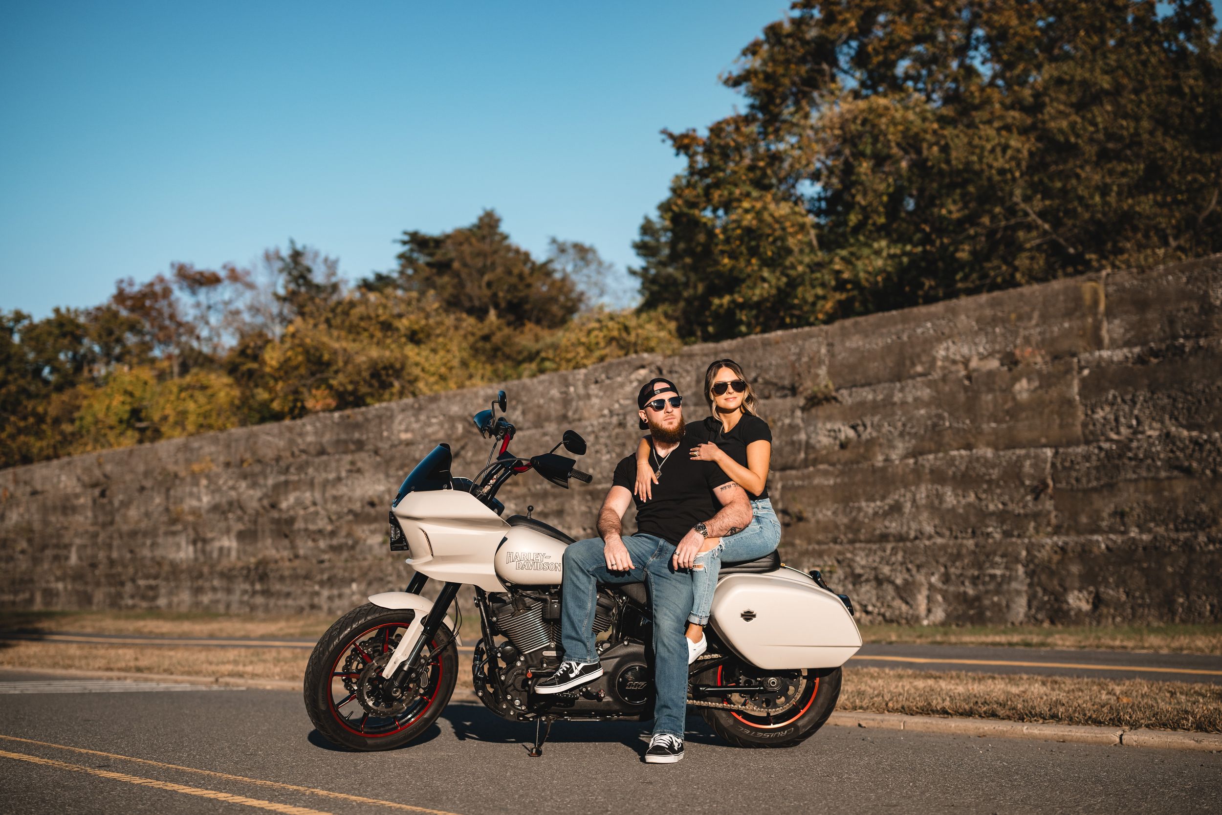 edgy engagement session portrait of a couple on their motorcycle leans into a curve on a scenic mountain road during a sunny autumn day.
