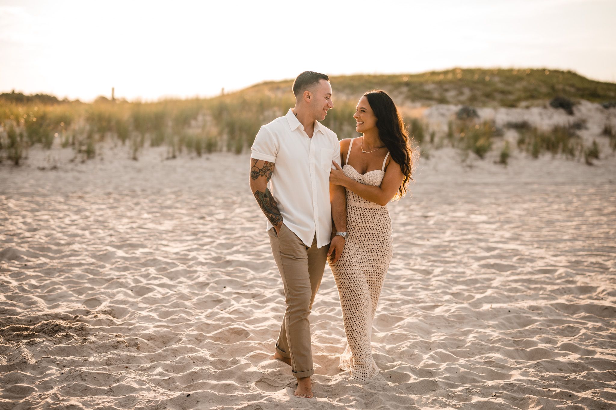 engagement session portrait Couple walking hand in hand on island beach state park during golden hour with dunes in the background.