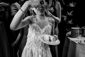 Bride in lace gown eating wedding cake in black and white photo at reception celebration.