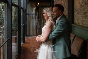 A romantic wedding couple shares an intimate moment in front of exposed brick walls and large windows.