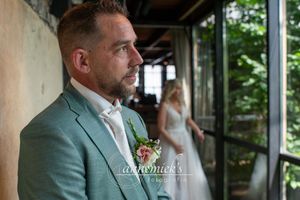 Wedding party members stand in a rustic venue with natural light streaming through windows.