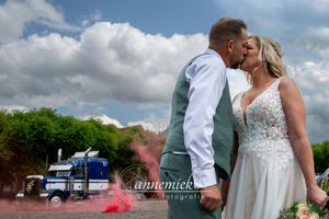 Wedding party poses outdoors on a sunny day with fluffy white clouds and a blue truck in the background.