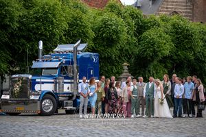 Large wedding party poses for group photos outdoors with a blue semi truck visible in the background.