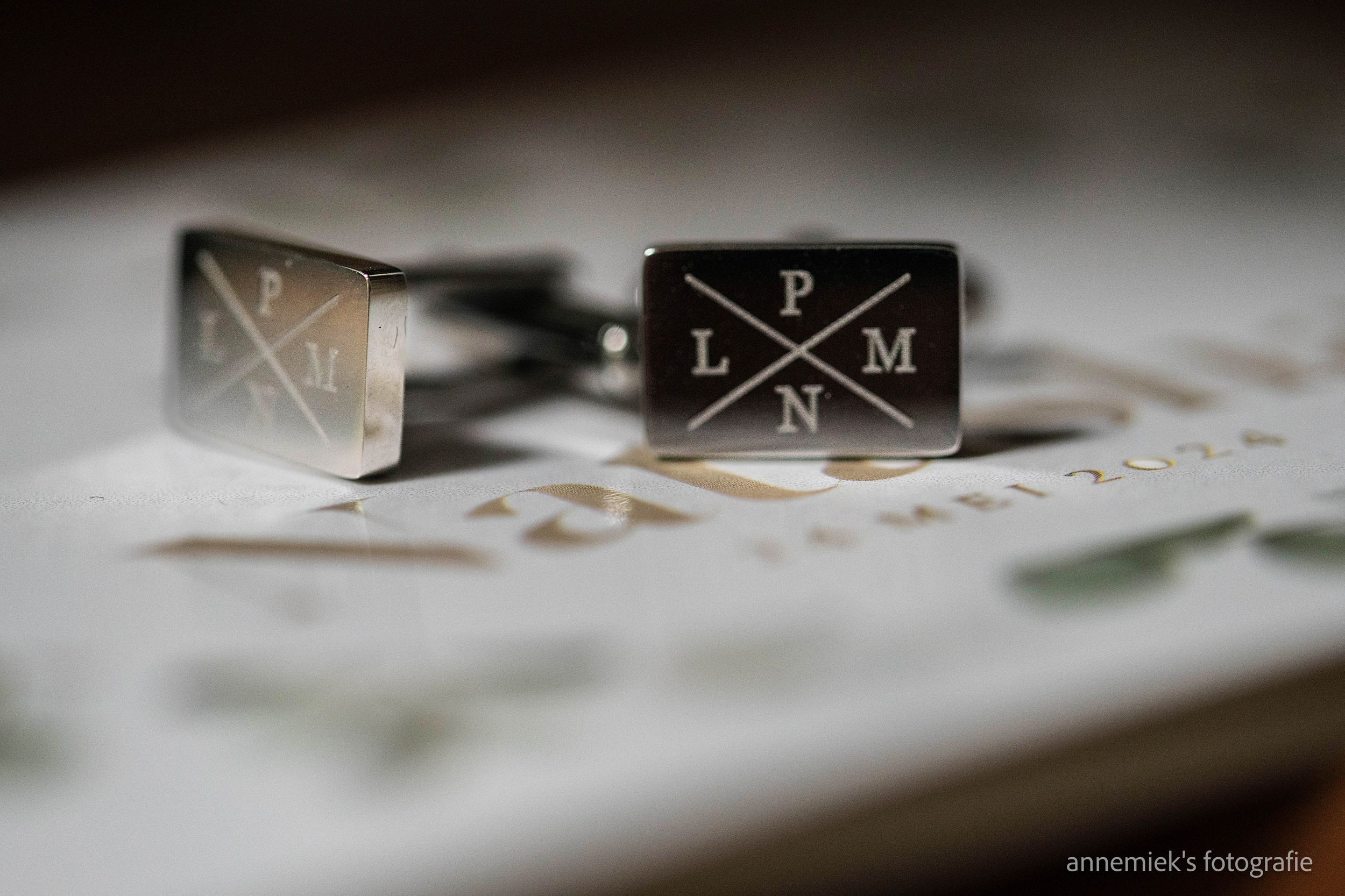 Silver engraved cufflinks with initials L, P, N, M resting on a wedding invitation card.