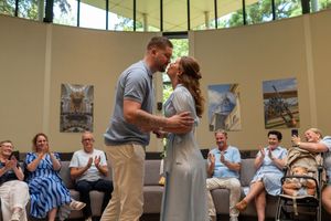 Couple shares a romantic kiss during an intimate wedding ceremony while guests applaud in a bright, art-filled venue.