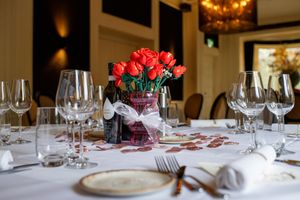 Elegant table settings with red roses and wine glasses at a formal dining event.