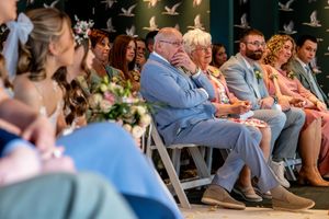 Emotional wedding guests seated in rows watching a ceremony, including an elderly couple in the front row.