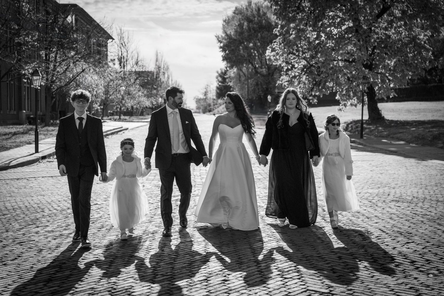 A wedding party walks together on a cobblestone street in black and white.
