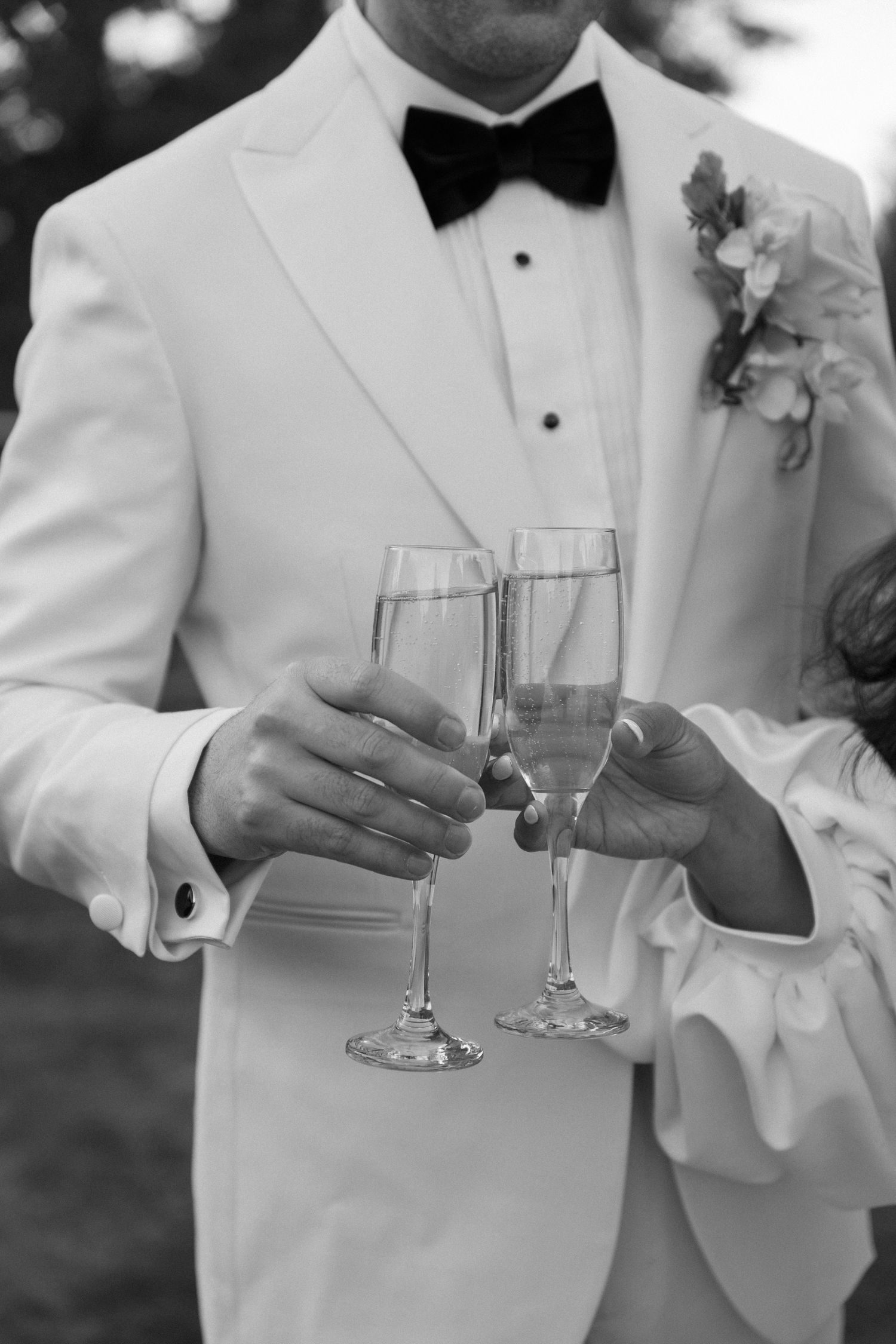 Wedding party in white tuxedos raise champagne glasses for a celebratory toast.