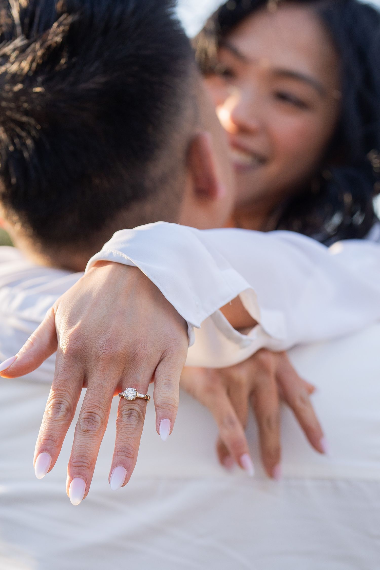 A series of hands with white manicured nails and a wedding ring shown against a white background in different poses.