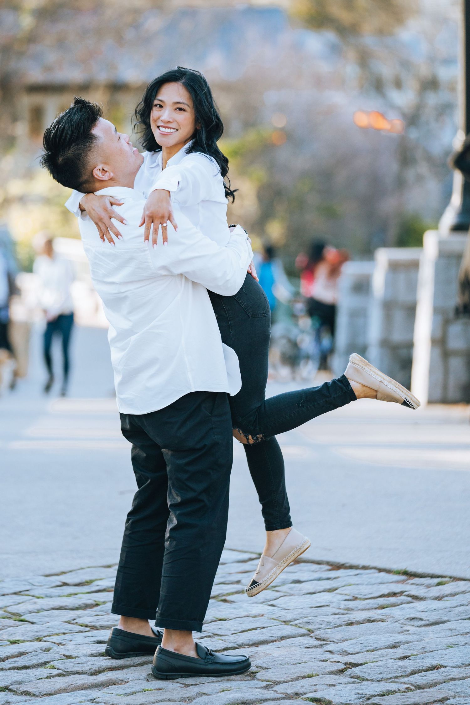 A joyful couple in matching white shirts share a playful moment on a cobblestone path.