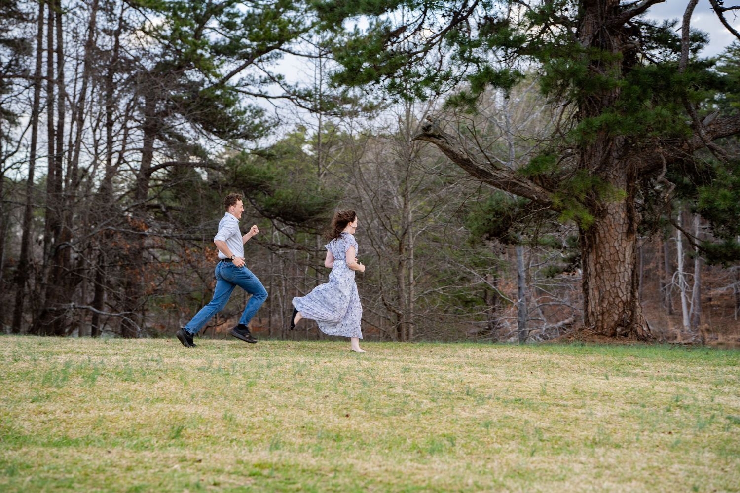 A couple runs playfully through a scenic wooded area on a bright autumn day.