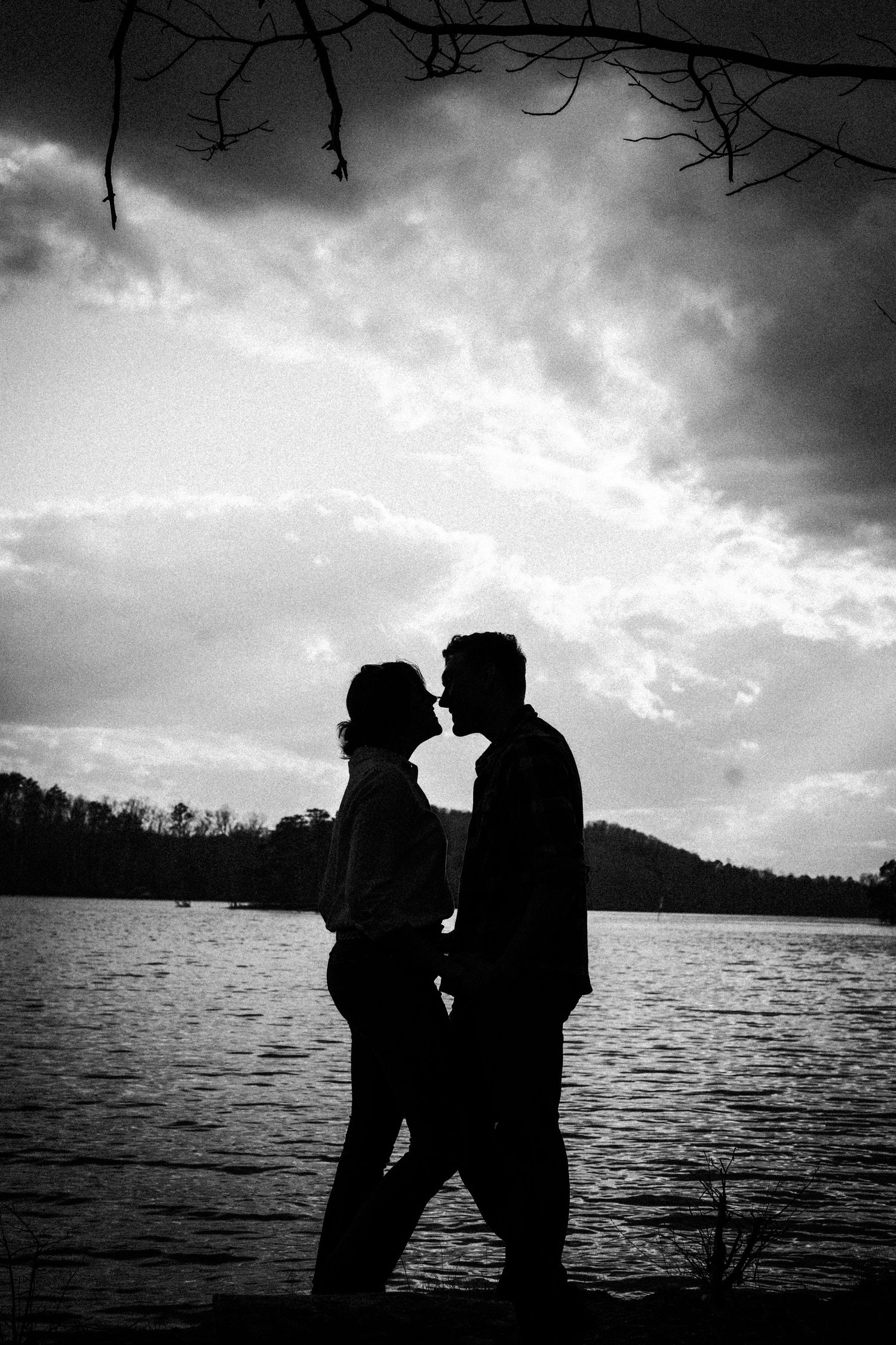 A romantic silhouette of a couple against a dramatic sky and lake at sunset.