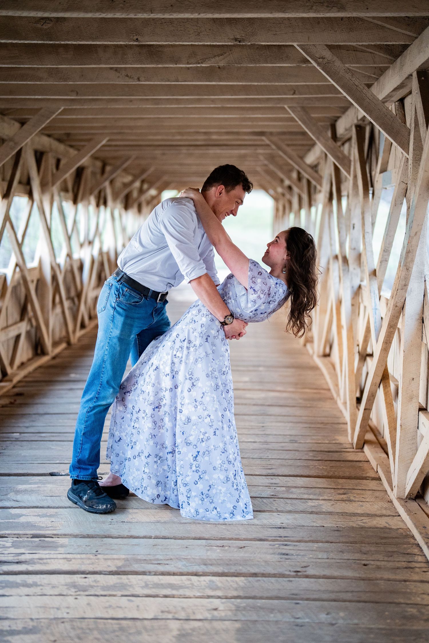 A romantic couple shares tender moments inside a rustic covered bridge with wooden beams and natural lighting.