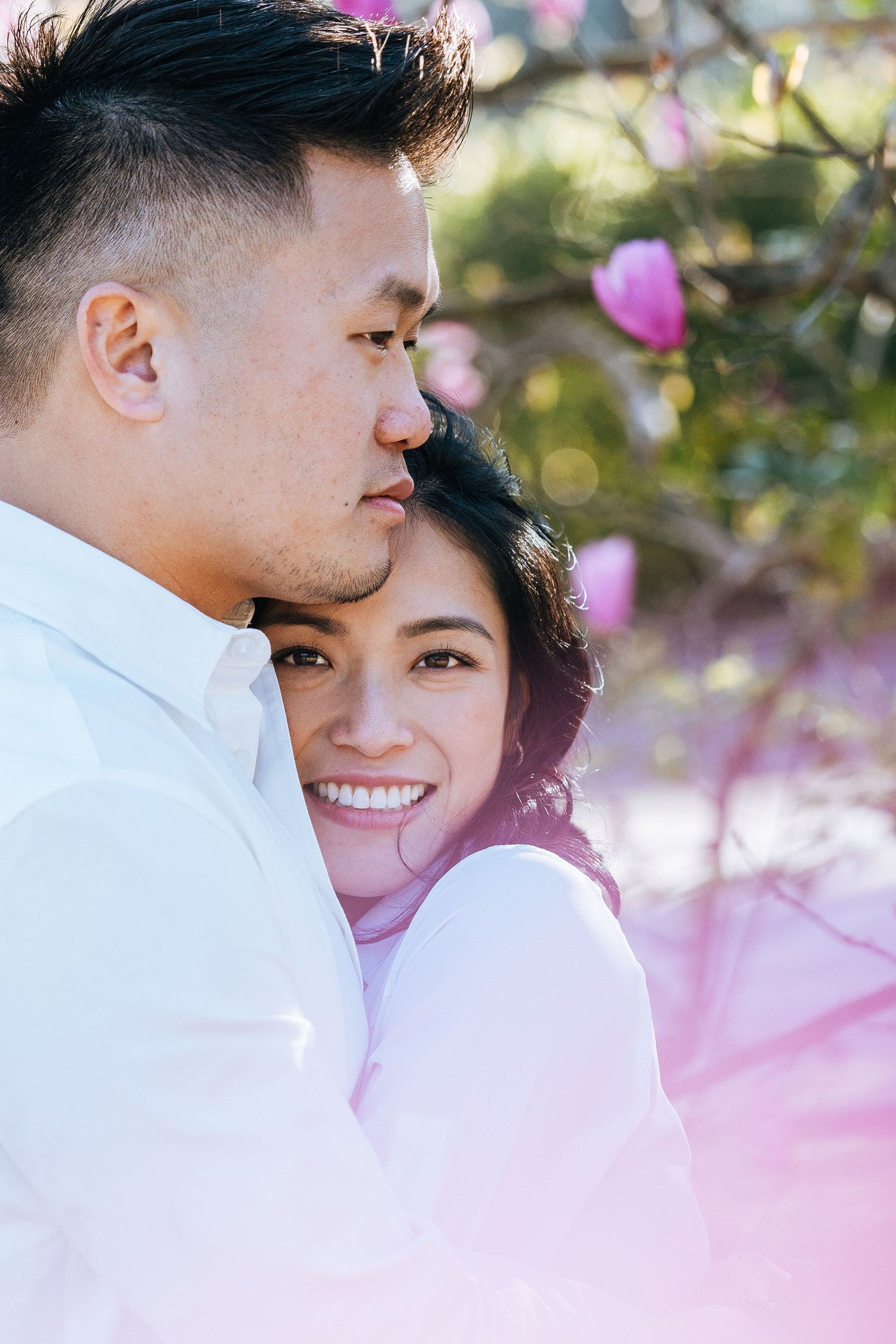 A romantic couple embraces among pink magnolia blossoms in a dreamy spring photoshoot.