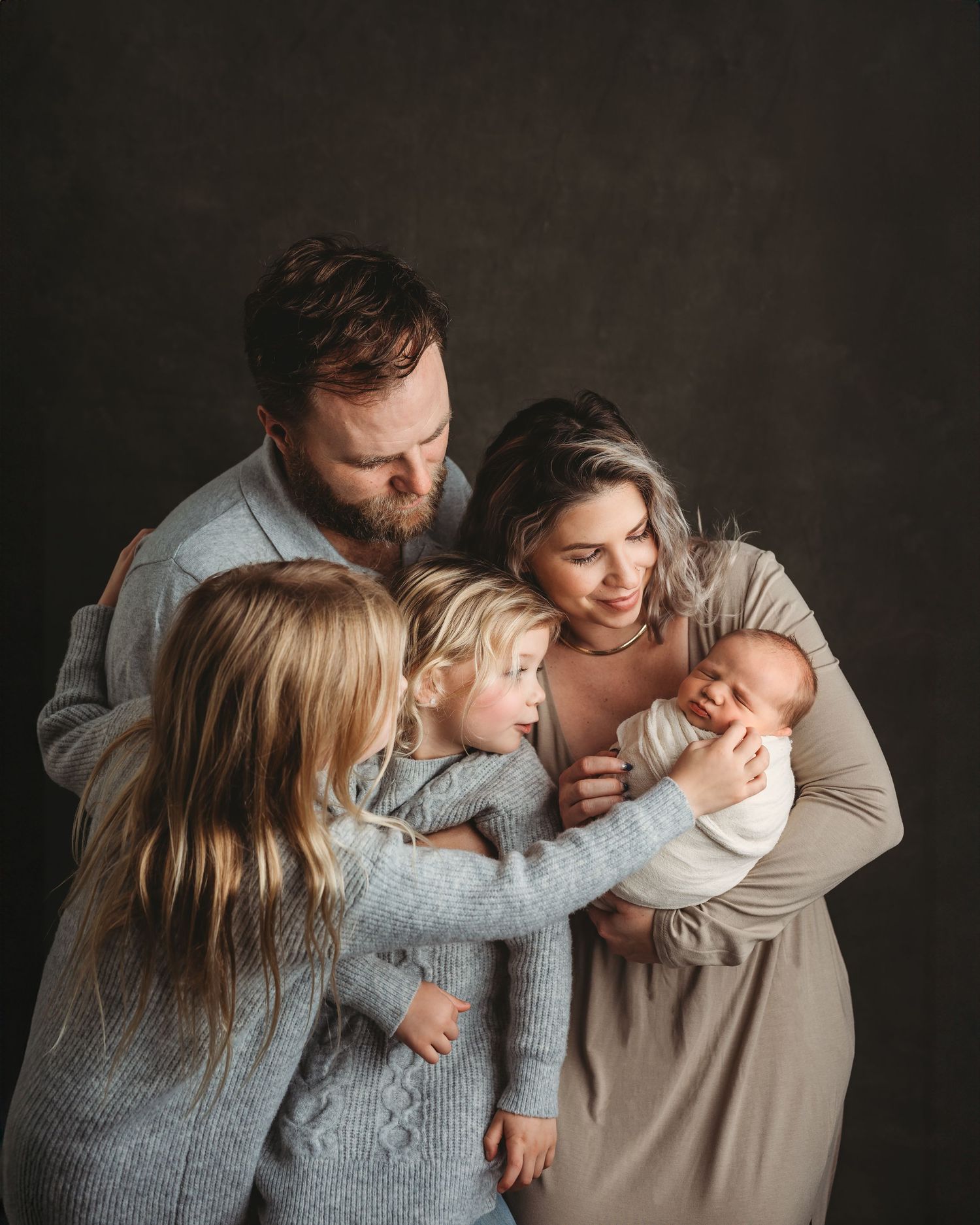 Family of five with newborn baby posing together in coordinating neutral outfits in studio.