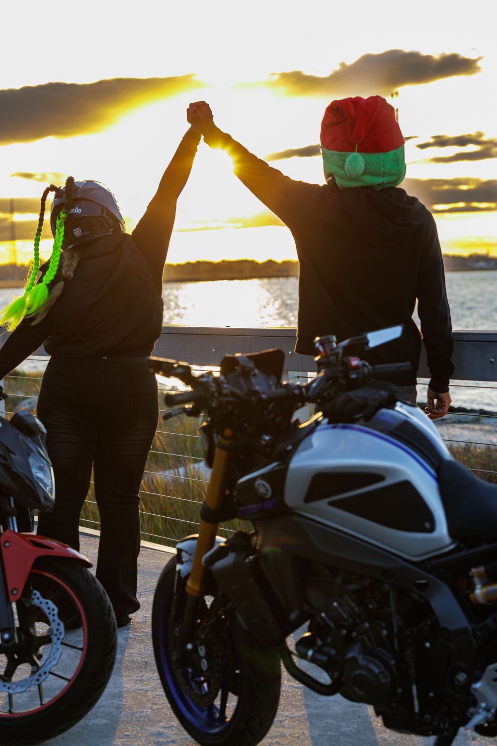 Silhouetted motorcycles against dramatic sunset sky at waterfront location.