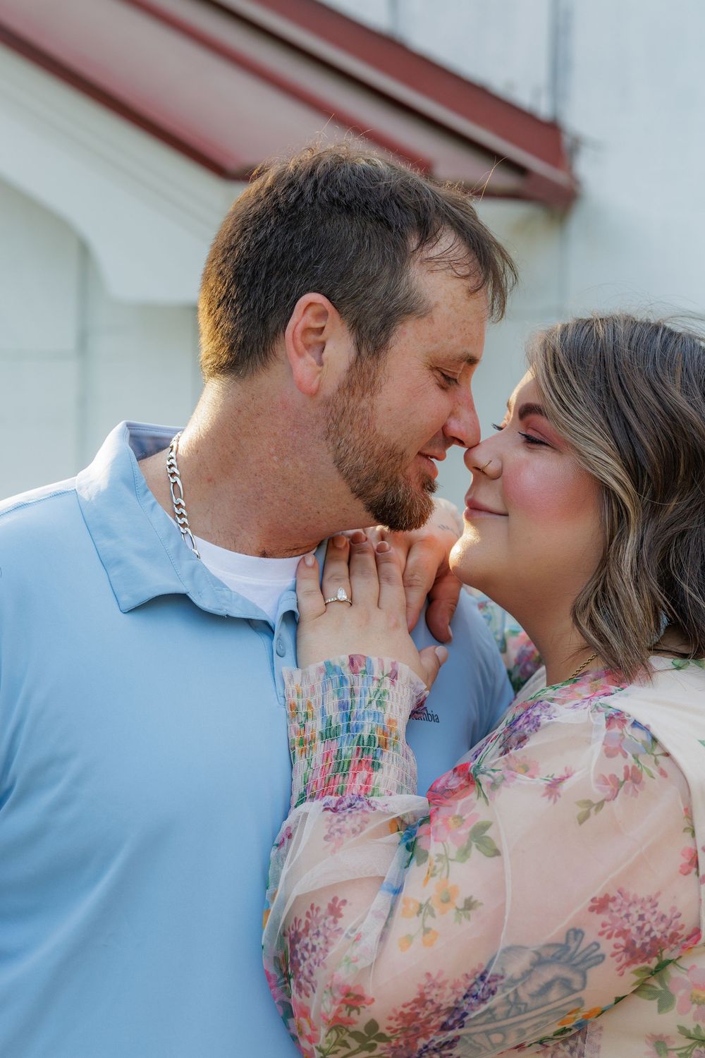 A couple in a romantic embrace share a tender moment, with the person in blue and person in floral pink clothing.