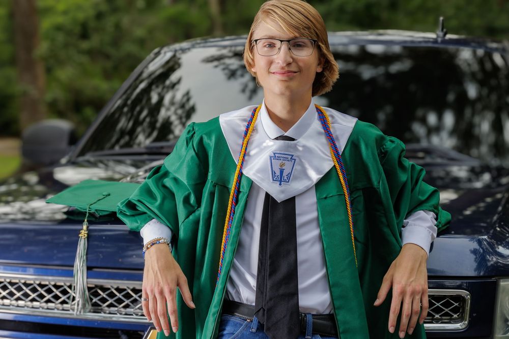 Graduate in green academic regalia posed against lattice background.