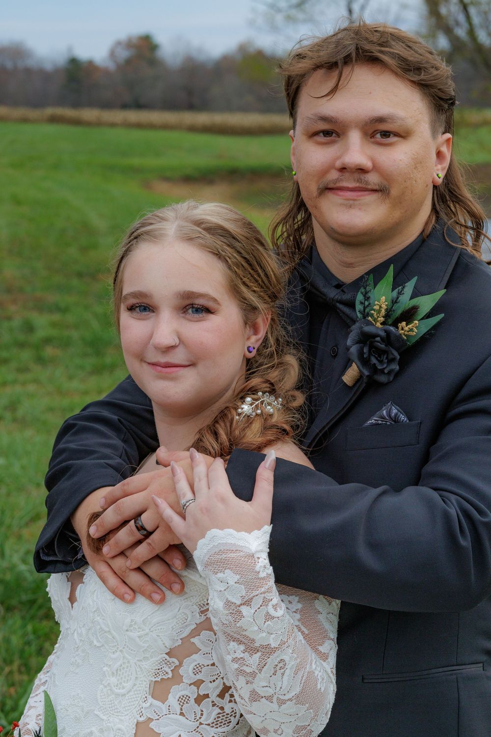 Wedding couple in traditional attire posing together in grassy outdoor setting.