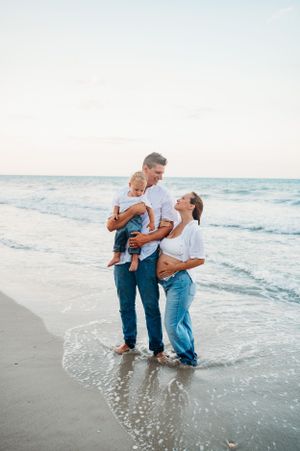 A family enjoys a tender moment together while standing in the ocean waves at sunset on a peaceful beach.