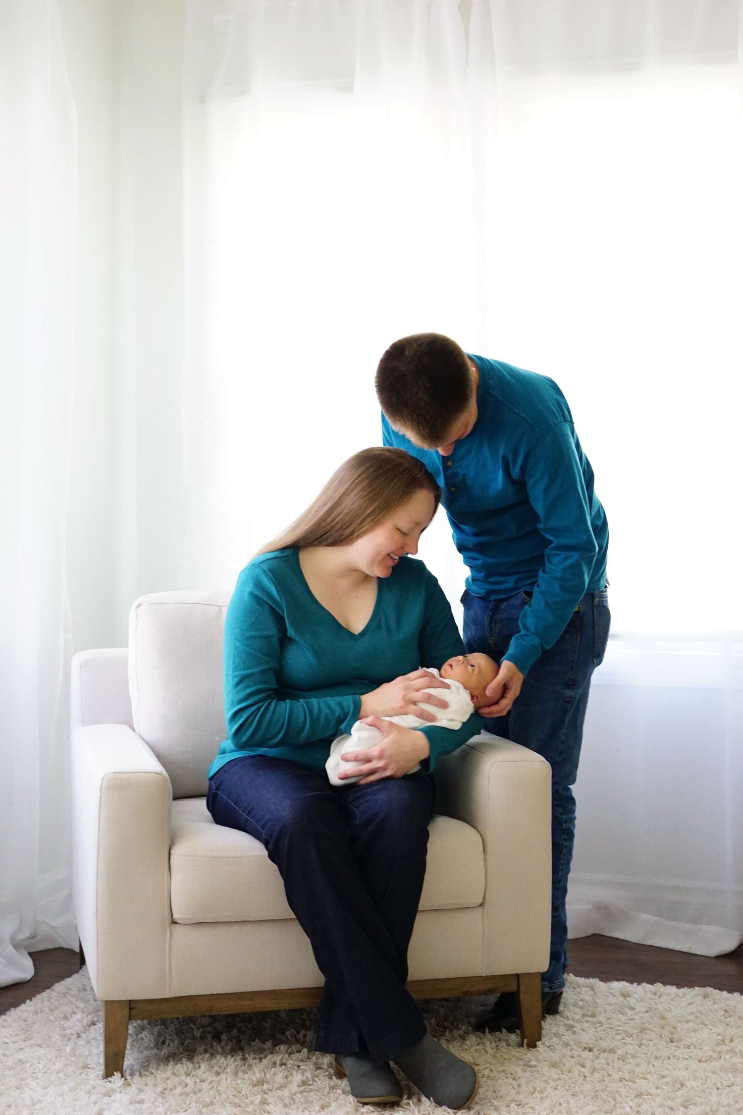 New parents share intimate moment with newborn baby in bright living room setting.