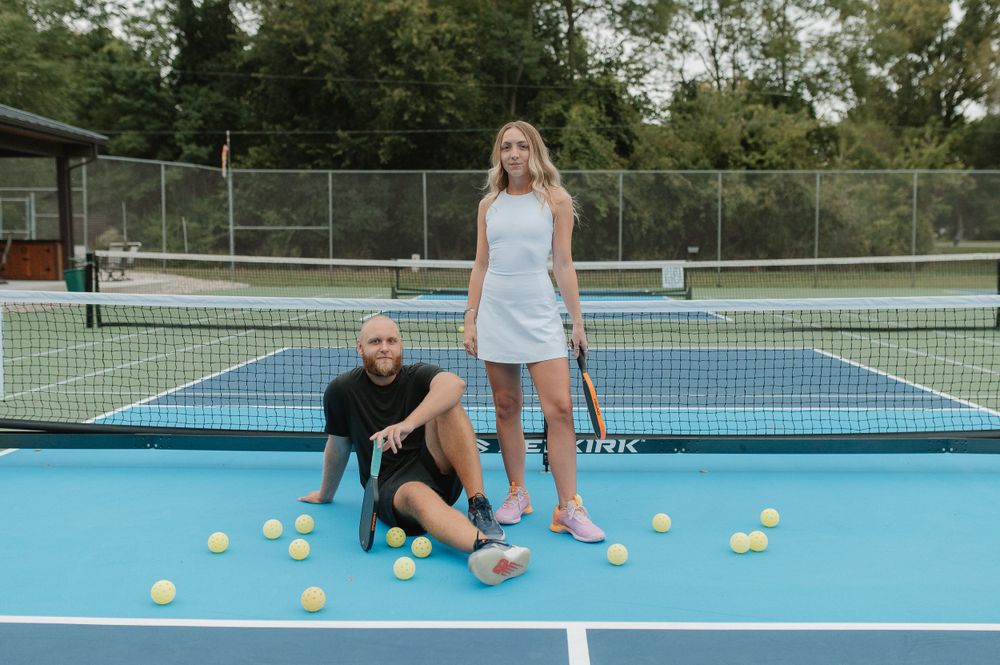 A creative engagement photoshoot on a tennis court with scattered yellow tennis balls.