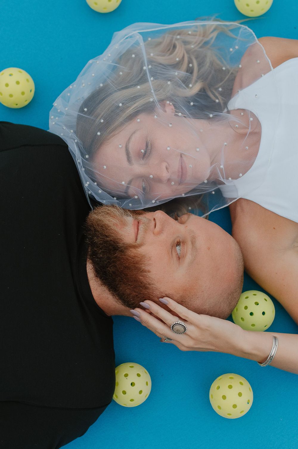 Artistic couple's portrait on blue background surrounded by yellow pickleball spheres.