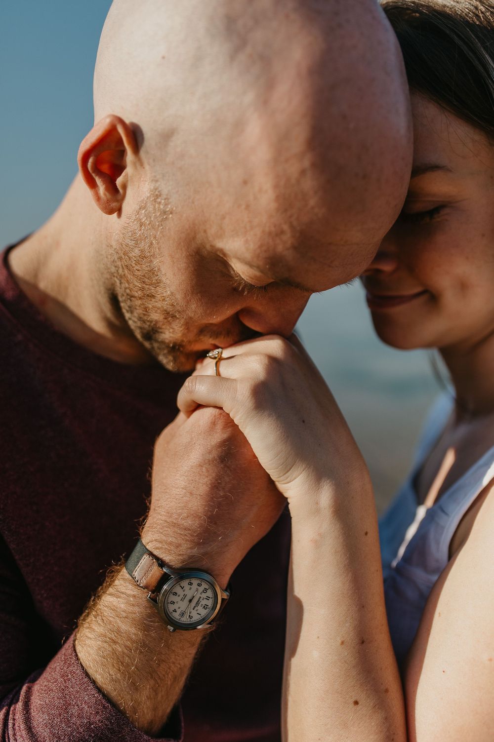 Intimate close-up photo of a couple sharing a tender moment as one kisses the other's hand at sunset.