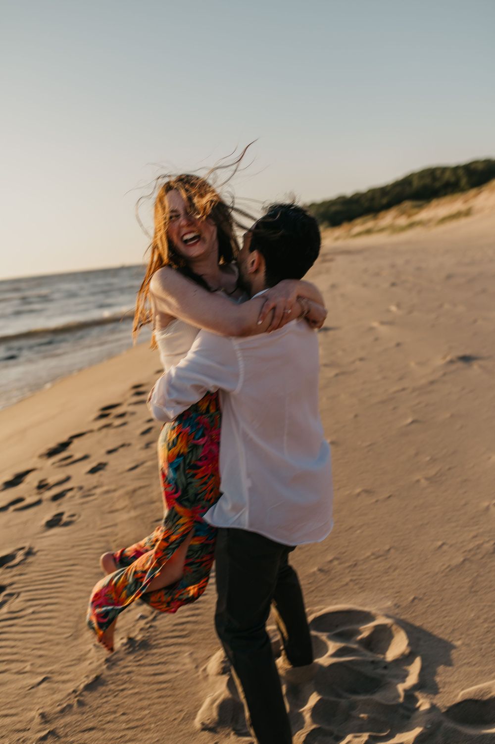 A joyful couple embraces and spins on a sandy beach at sunset, creating playful shadows on the sand.
