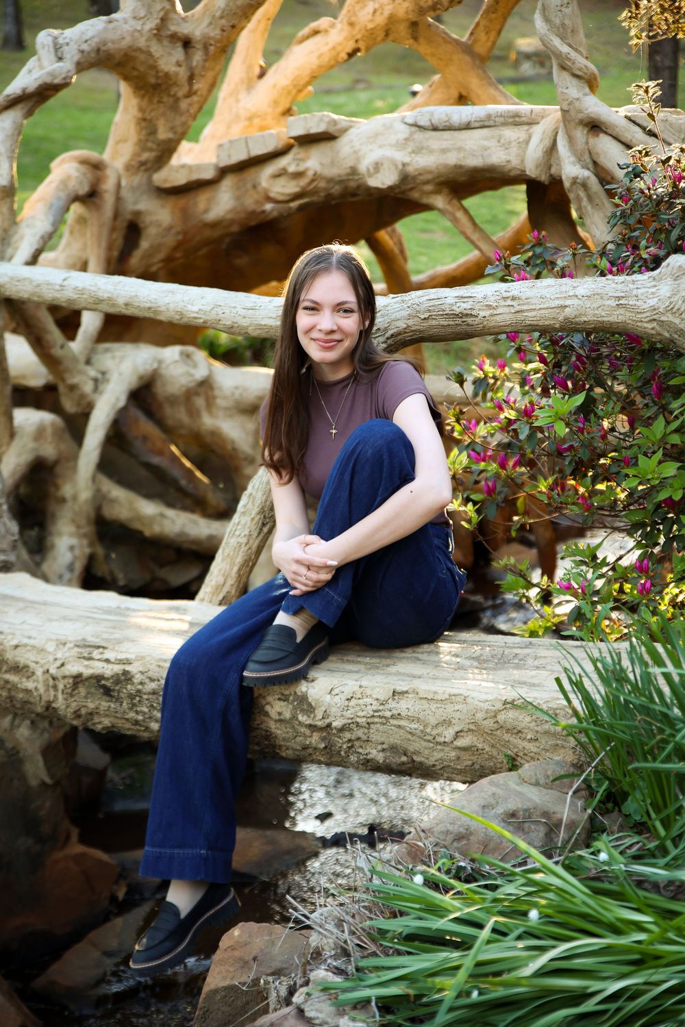 A teenage girl smiles while sitting on a stone bridge surrounded by lush garden greenery.