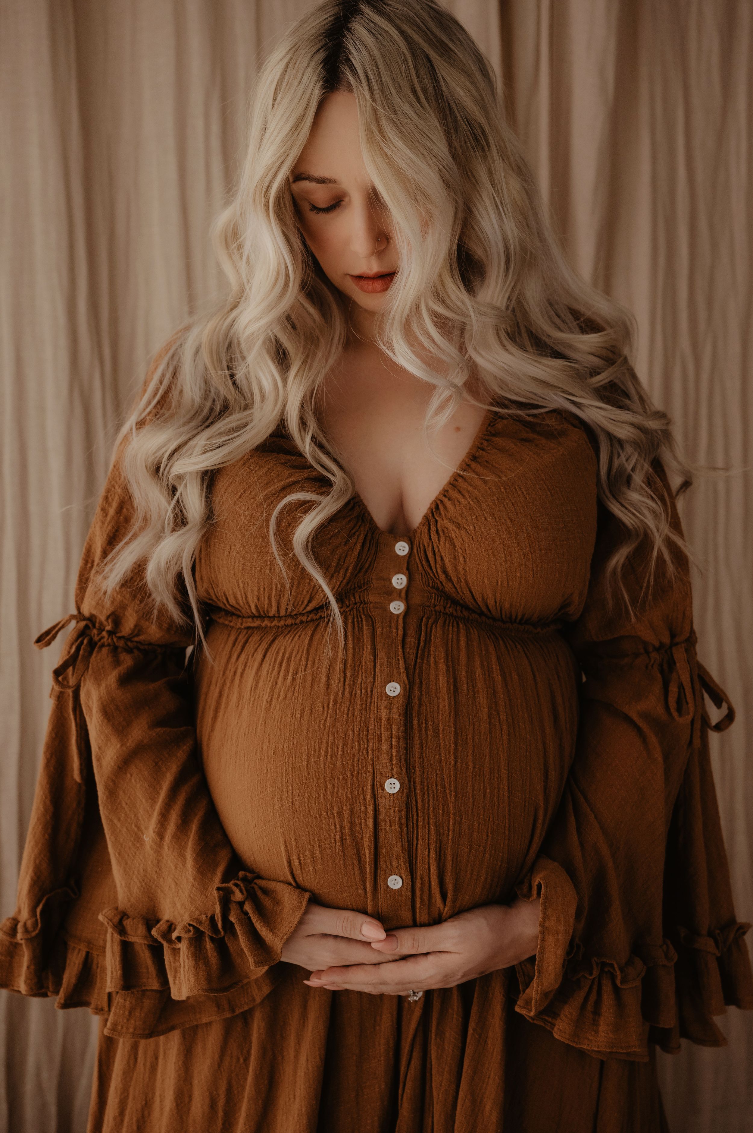 Woman wearing brown ruffled dress in atmospheric portrait setting.