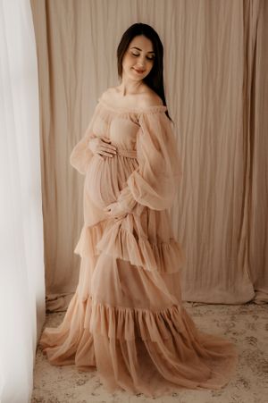 Flowing peach-colored maternity gown with ruffled tiers captured in romantic studio setting.