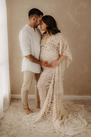 Intimate maternity portrait of couple in white and lace sharing tender moment.