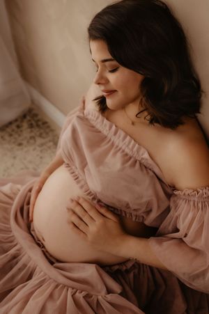 Dreamy maternity photo with woman in pink dress cradling baby bump.