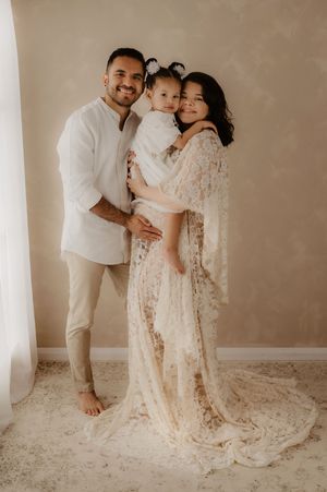 Beautiful family portrait in cream and white lace outfits against neutral background.